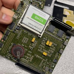 ZP-KOMP Przemysław Zajączkowski - Szczegółowe zbliżenie na zieloną płytę główną komputera z widocznymi elementami elektronicznymi, w tym baterią pastylkową i kartą CompactFlash 512MB, trzymaną w dłoni.