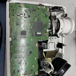 ZP-KOMP Przemysław Zajączkowski - Otwarty projektor z widoczną płytą główną, elementami optycznymi i wentylatorem podczas naprawy, ukazujący skomplikowaną budowę urządzenia.