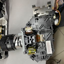 ZP-KOMP Przemysław Zajączkowski - Rozłożony projektor z widocznymi elementami optycznymi, elektroniką i wentylatorem, leżący na szarym stole.