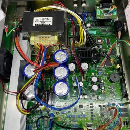 ZP-KOMP Przemysław Zajączkowski - Otwarta obudowa urządzenia elektronicznego z widoczną zieloną płytą główną, kondensatorami, transformatorem i licznymi kablami w różnych kolorach.