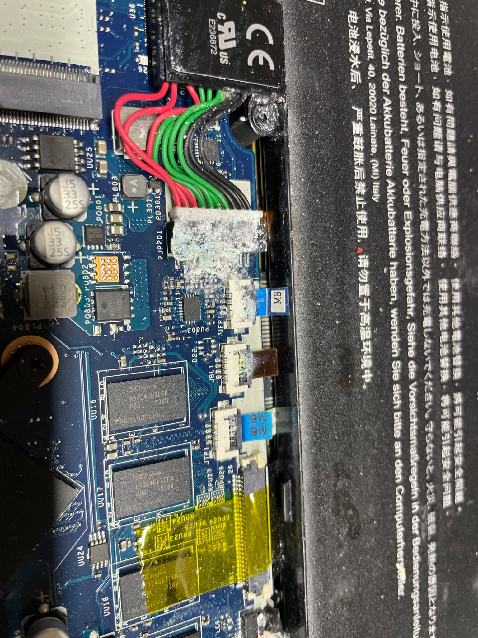 Detaliczne zbliżenie na płytę główną laptopa z widocznymi elementami elektronicznymi, przewodami w kolorach czerwonym, zielonym i czarnym oraz złączami, pokrytymi białym nalotem, prawdopodobnie po...