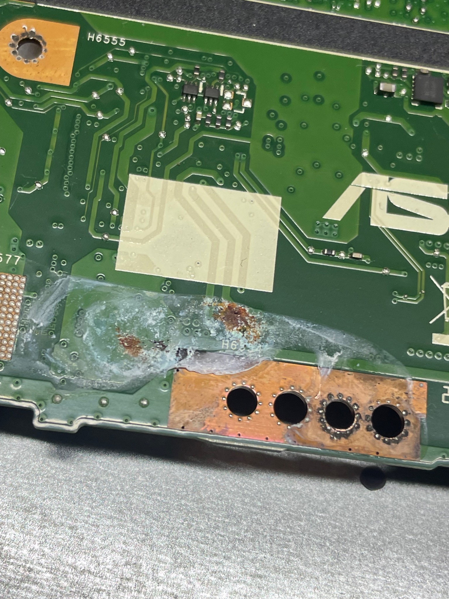 Uszkodzona płyta główna laptopa ASUS z widocznymi śladami korozji i zalania w pobliżu układu chłodzenia.