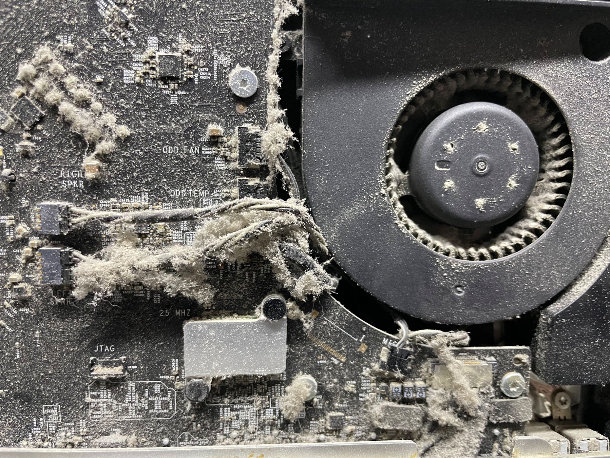 Wnętrze komputera stacjonarnego, mocno zakurzona płyta główna i wentylator chłodzenia. Widoczne elementy elektroniki pokryte grubą warstwą kurzu i pyłu.