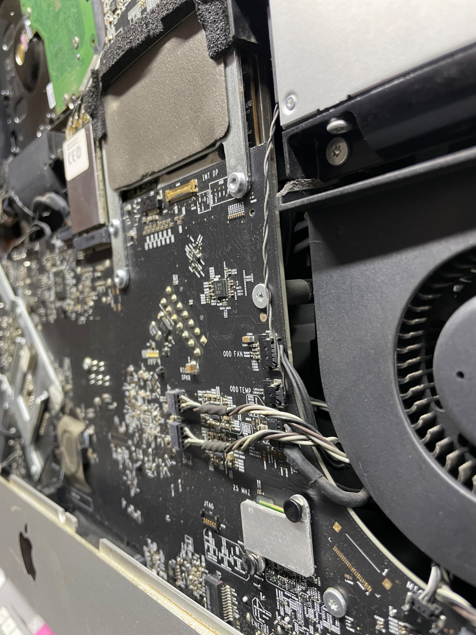 Wnętrze rozkręconego komputera iMac z widoczną płytą główną, wentylatorem chłodzącym i dyskiem twardym, detale elektroniki i okablowania.