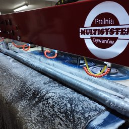 Multisystem Jarosław Stosio - Automatyczna maszyna z logiem 'Pralnia Multisystem Dywanów' w trakcie czyszczenia dywanu, widoczne obracające się szczotki i piana.