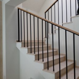 Ol-stal - Wewnętrzna klatka schodowa z balustradą z czarnych prętów i drewnianym poręczą, widok z dołu na jasne marmurowe stopnie.