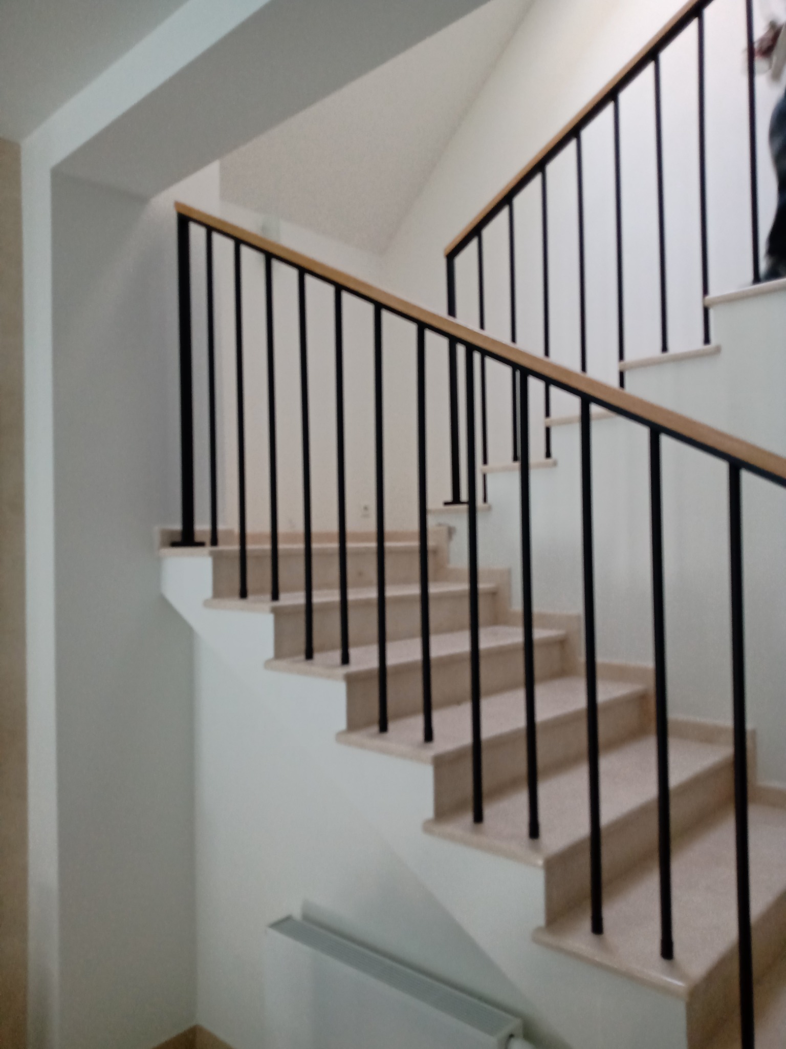 Wewnętrzna klatka schodowa z balustradą z czarnych prętów i drewnianym poręczą, widok z dołu na jasne marmurowe stopnie.