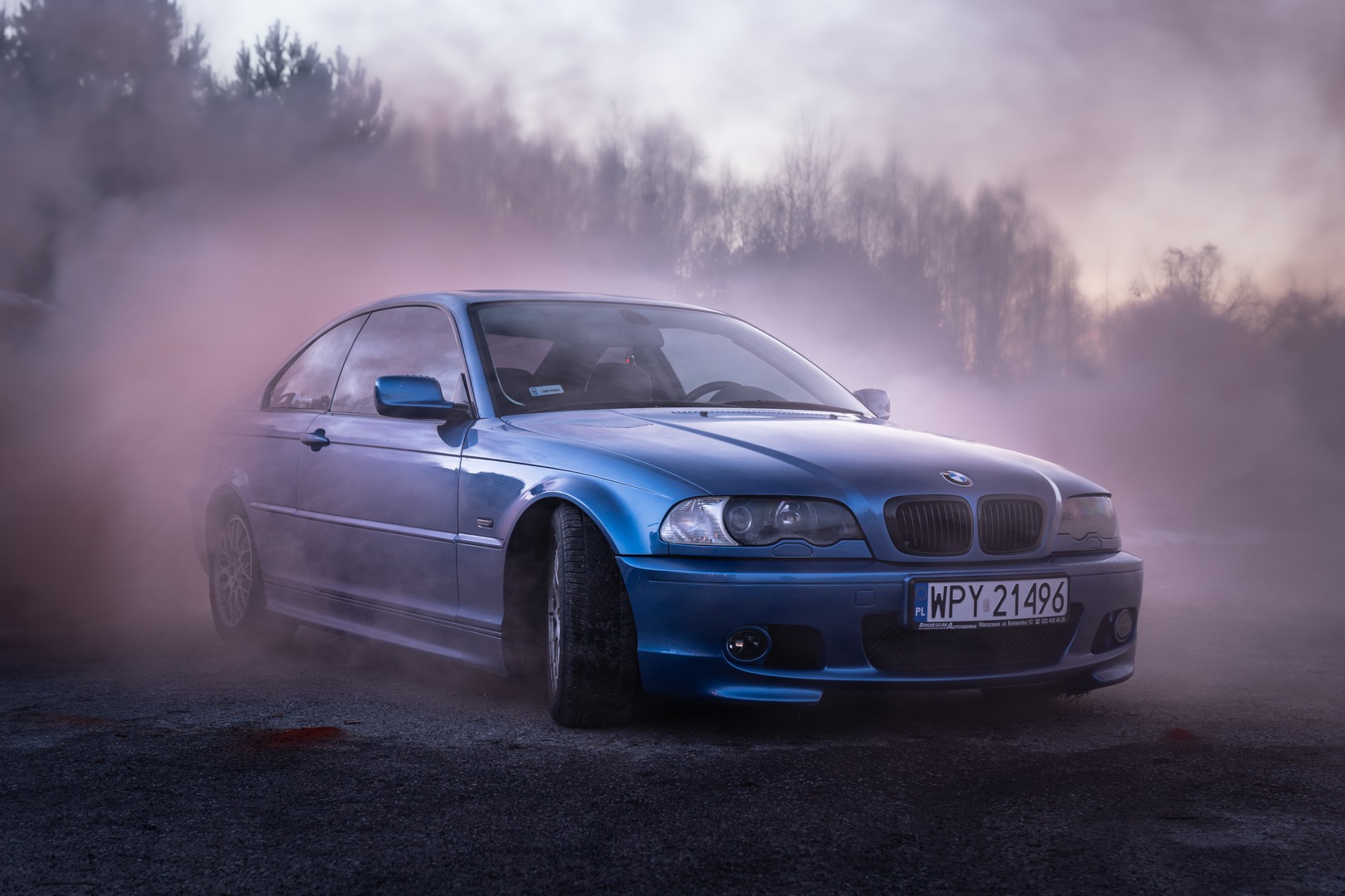Niebieskie BMW E46 coupe w oparach dymu na tle drzew, tablica rejestracyjna WPY 21496.