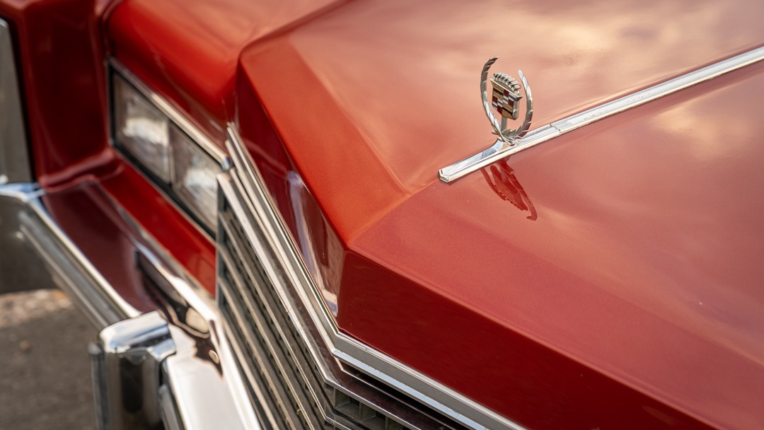 Czerwony Cadillac z chromowanym grillem i ozdobnym logo na masce, odbijającym niebo.