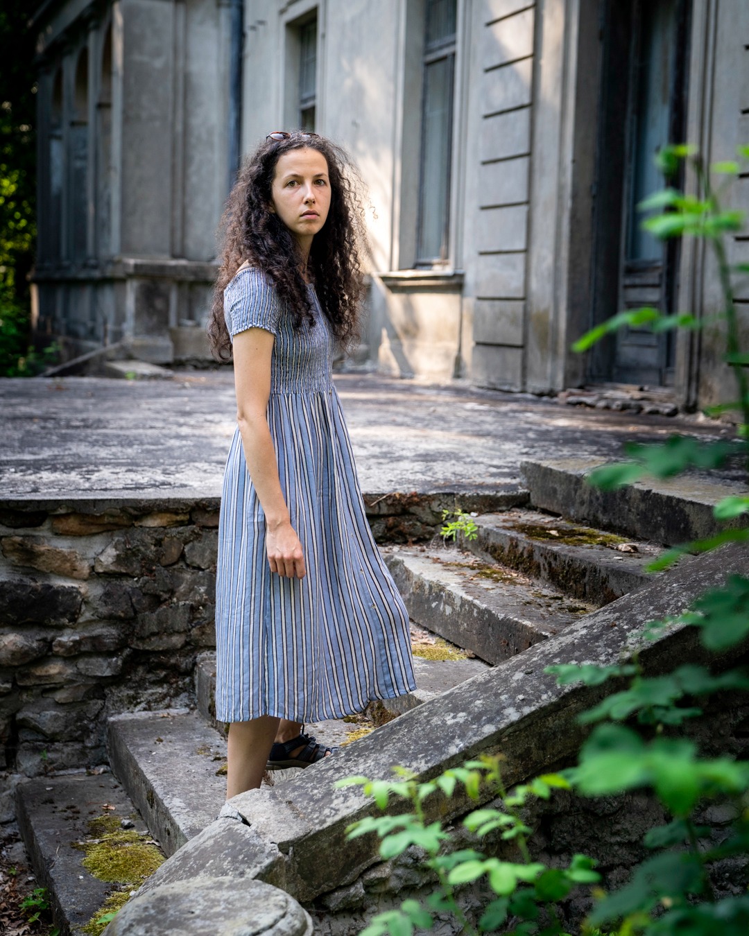 Kobieta w paski sukience pozuje na zniszczonych kamiennych schodach przed starym budynkiem z kolumnami.