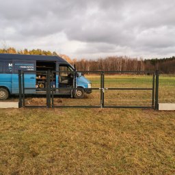 Montaż Bram i ogrodzeń Arendt Rafał - Zamknięta brama panelowa z metalową siatką i prostym zamkiem, na tle łąki i zaparkowanego firmowego busa z otwartymi drzwiami, widok z poziomu gruntu, pochmurne niebo.
