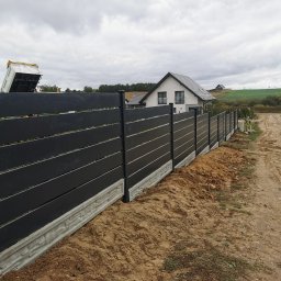 Montaż Bram i ogrodzeń Arendt Rafał - Nowoczesne, czarne ogrodzenie z poziomych desek na betonowej podmurówce, widok z boku, w tle dom jednorodzinny i wywrotka z piaskiem.