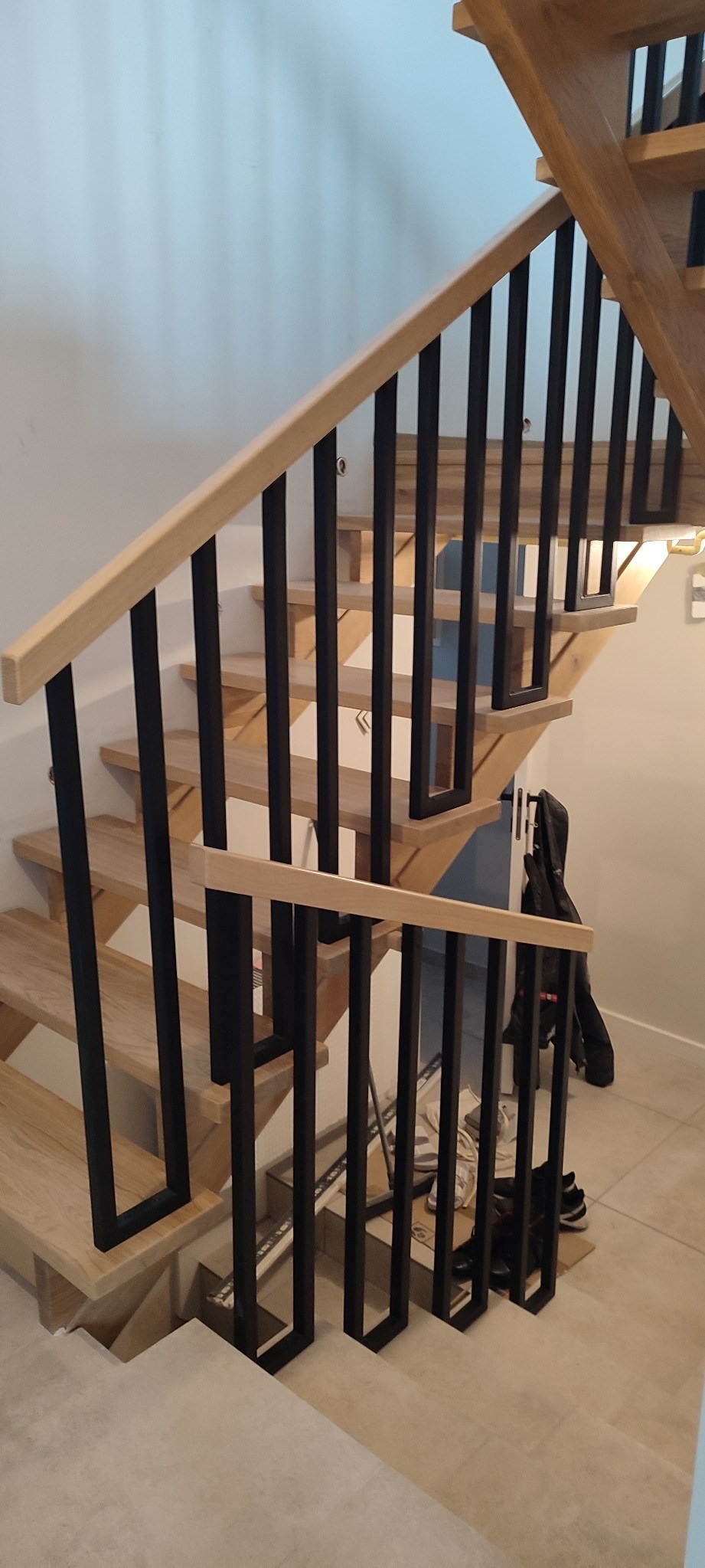 Drewniane schody z czarną, metalową balustradą o minimalistycznym designie, widok z dołu, z widocznymi elementami konstrukcyjnymi i jasnym oświetleniem.