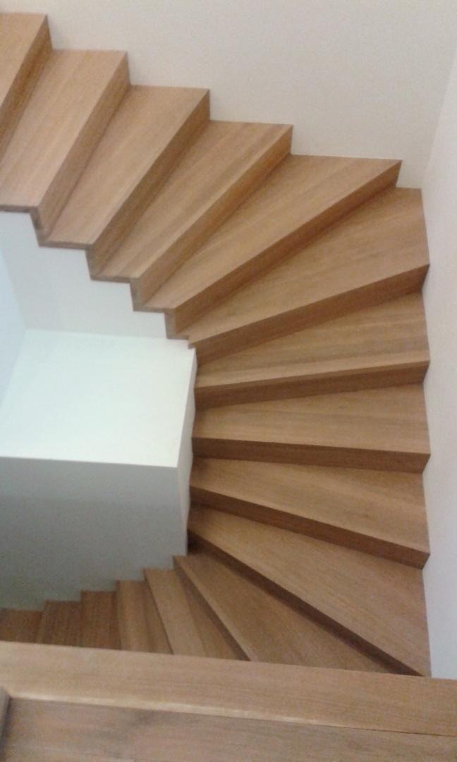 Wewnętrzne, spiralne schody z jasnego drewna, widok z góry, minimalistyczny design z białymi ścianami.