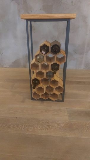 Drewniany regał na wino w kształcie plastra miodu, umieszczony w metalowej ramie, na podłodze z paneli.