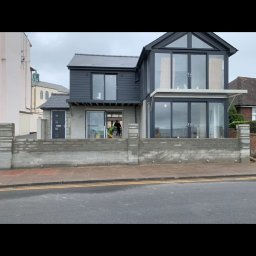 VIKING - Dwupiętrowy dom z szarą elewacją i dużymi oknami na parterze, w trakcie prac wykończeniowych, widoczny pracownik wewnątrz budynku.