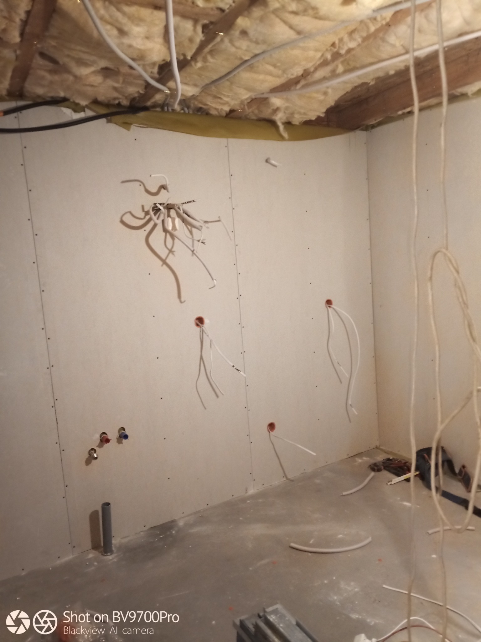 Wnętrze w trakcie prac wykończeniowych: ściany pokryte płytami gipsowo-kartonowymi z wystającymi przewodami elektrycznymi i rurami instalacji wodnej, sufit ocieplony wełną mineralną, widoczne...