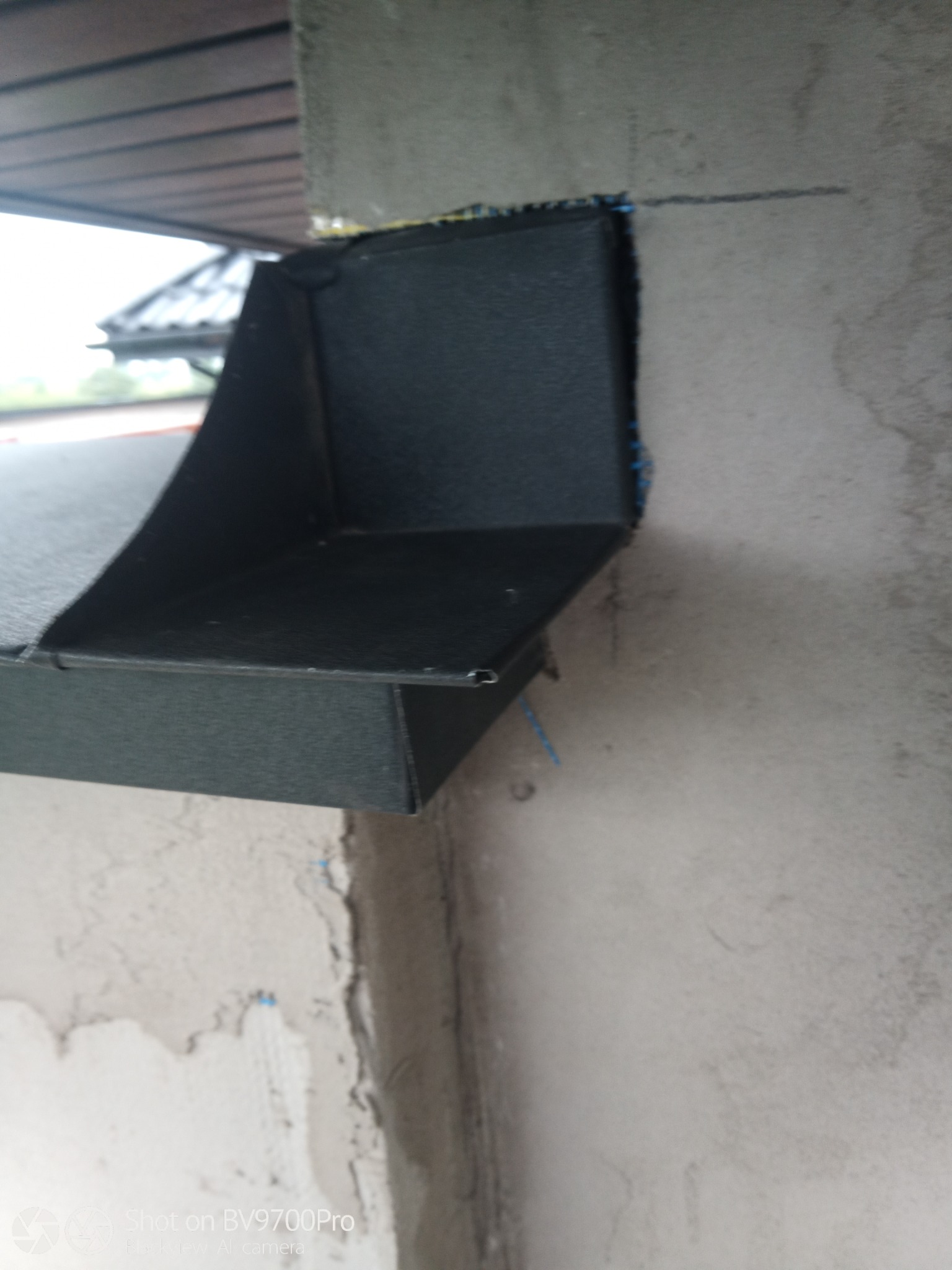 Zamontowana, czarna obróbka blacharska przy krawędzi dachu, widoczna na tle surowego, szarego betonu.