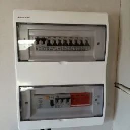 Zamknięta, biała skrzynka elektryczna Elektro-Plast z widocznymi bezpiecznikami IDEAL i listwą Schalinger, zamontowana na jasnej ścianie w trakcie prac wykończeniowych.