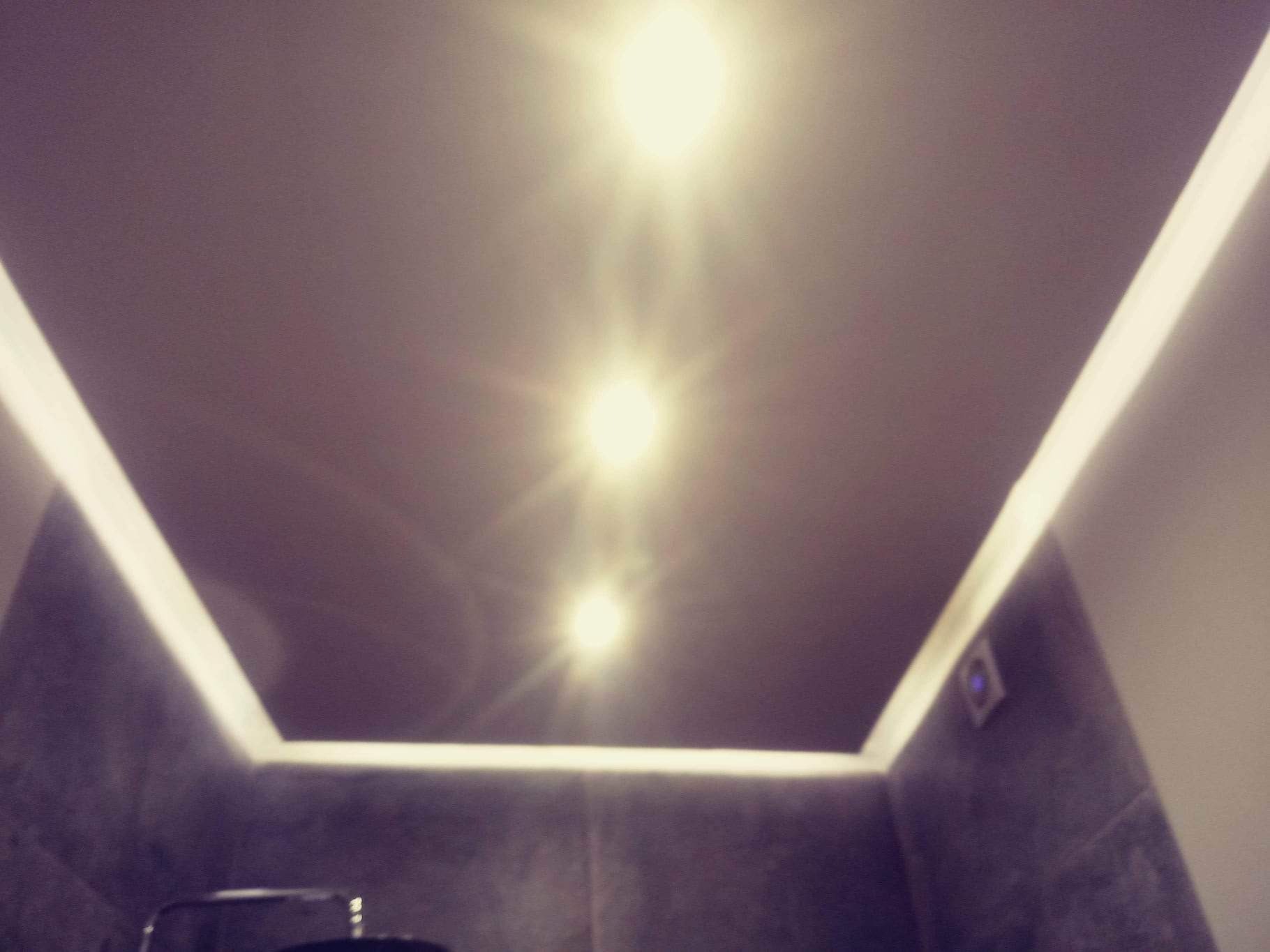 Sufit w łazience z trzema punktowymi źródłami światła i oświetleniem LED wzdłuż krawędzi, widoczny fragment ściany wykończonej płytkami imitującymi kamień.