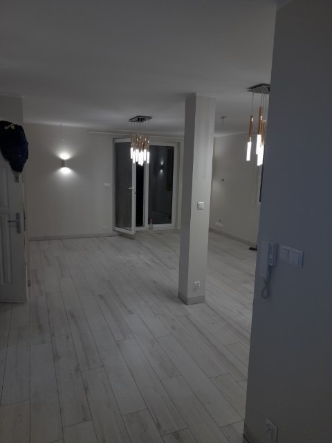 Jasne, przestronne wnętrze po remoncie z nową, drewnopodobną podłogą, nowoczesnym oświetleniem sufitowym i otwartym balkonem.