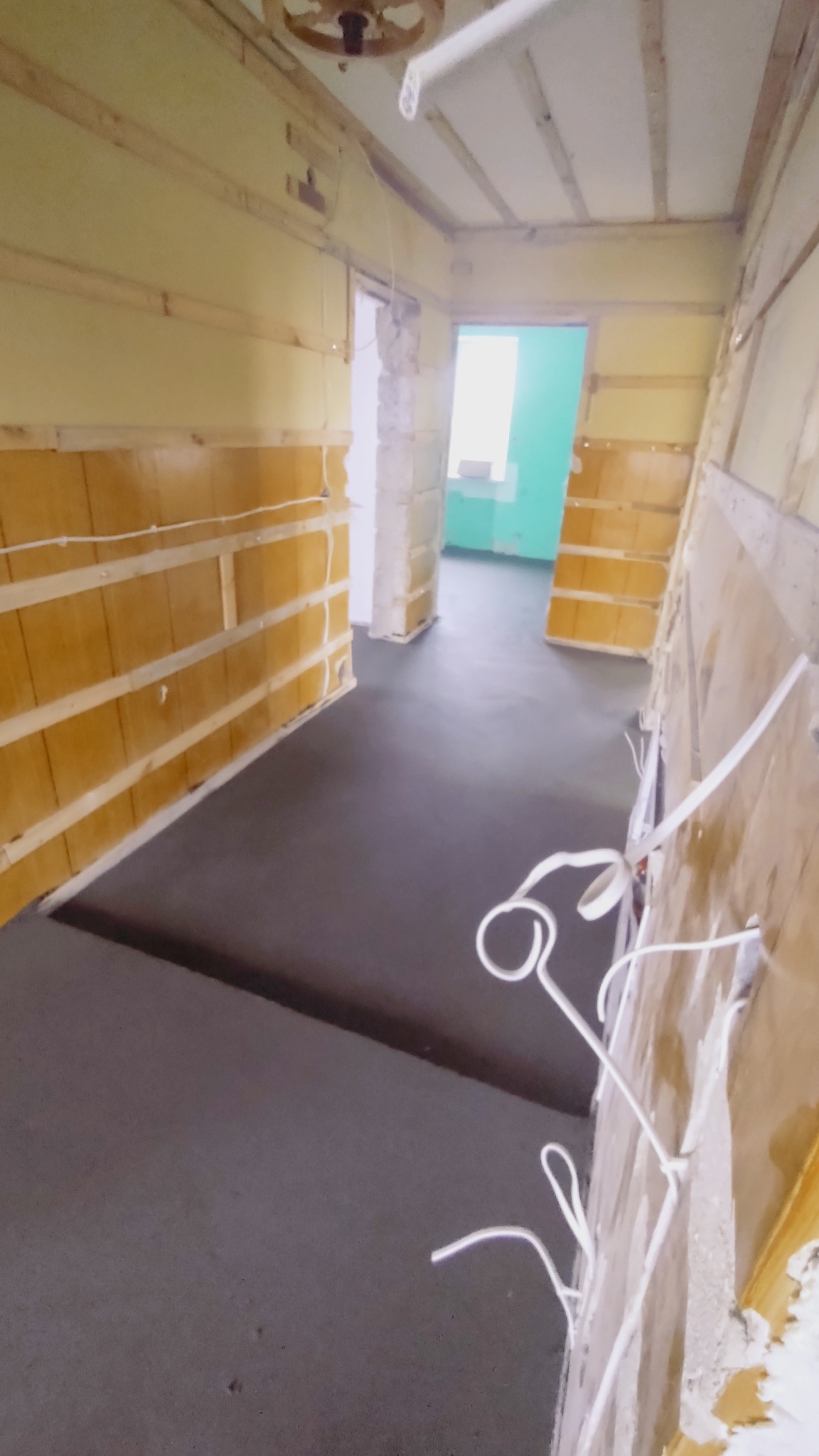 Wnętrze w trakcie prac przygotowawczych: wyrównana, ciemnoszara wylewka na podłodze, ściany z widoczną drewnianą konstrukcją i przewodami elektrycznymi, surowy stan wykończenia.