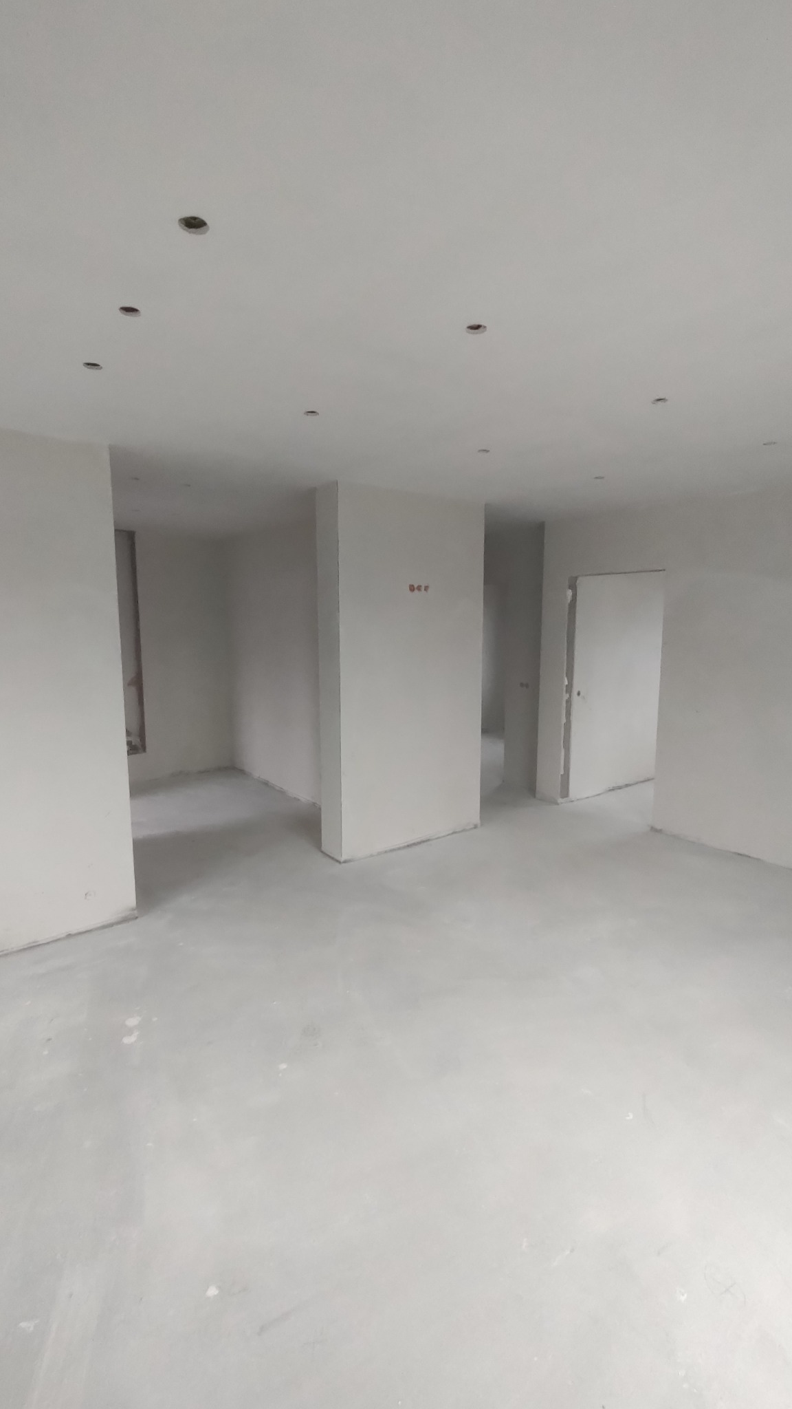 Pusty, wyszpachlowany pokój w trakcie remontu z przygotowanymi otworami na oświetlenie w suficie i surową podłogą.