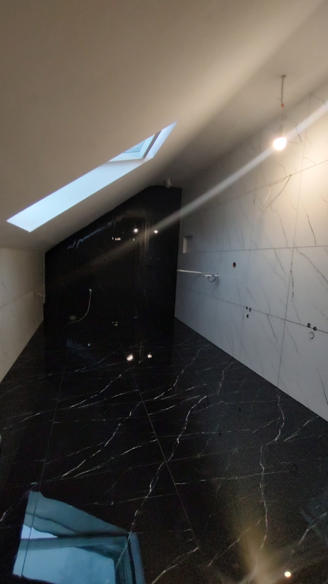 Wykończone poddasze z czarną marmurową podłogą i częściowo wykończonymi białymi ścianami z marmurowym wzorem, widoczne otwory na gniazdka elektryczne i okno dachowe.