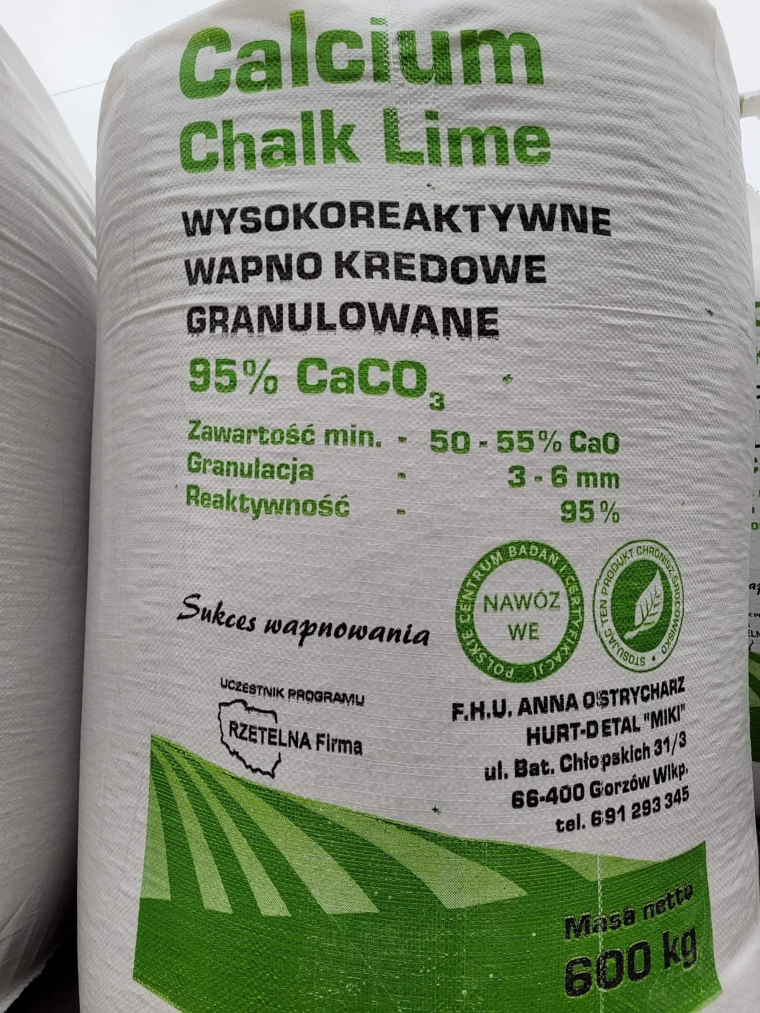 Wielki, biały worek z wapnem kredowym granulowanym Calcium Chalk Lime, z widocznymi informacjami o składzie, granulacji, rekatywności i wadze 600 kg, oraz logo 'Rzetelna Firma' i certyfikatami...