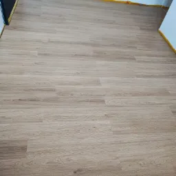 Jasne panele podłogowe z widoczną strukturą drewna, zabezpieczone żółtą folią przy ścianach, ułożone w nowym pomieszczeniu.