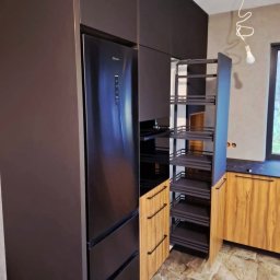 PPHU REDZIMSKI PIOTR REDZIMSKI - Nowoczesna kuchnia na wymiar: ciemne, matowe fronty szafek, wysuwana cargo, lodówka w zabudowie, drewnopodobne akcenty. Minimalistyczny design, funkcjonalność.