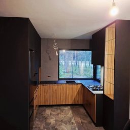 PPHU REDZIMSKI PIOTR REDZIMSKI - Nowoczesna kuchnia w odcieniach brązu i czerni z dużym oknem. Drewniane fronty szafek kontrastują z ciemnymi ścianami i blatem. Na podłodze płytki imitujące kamień.