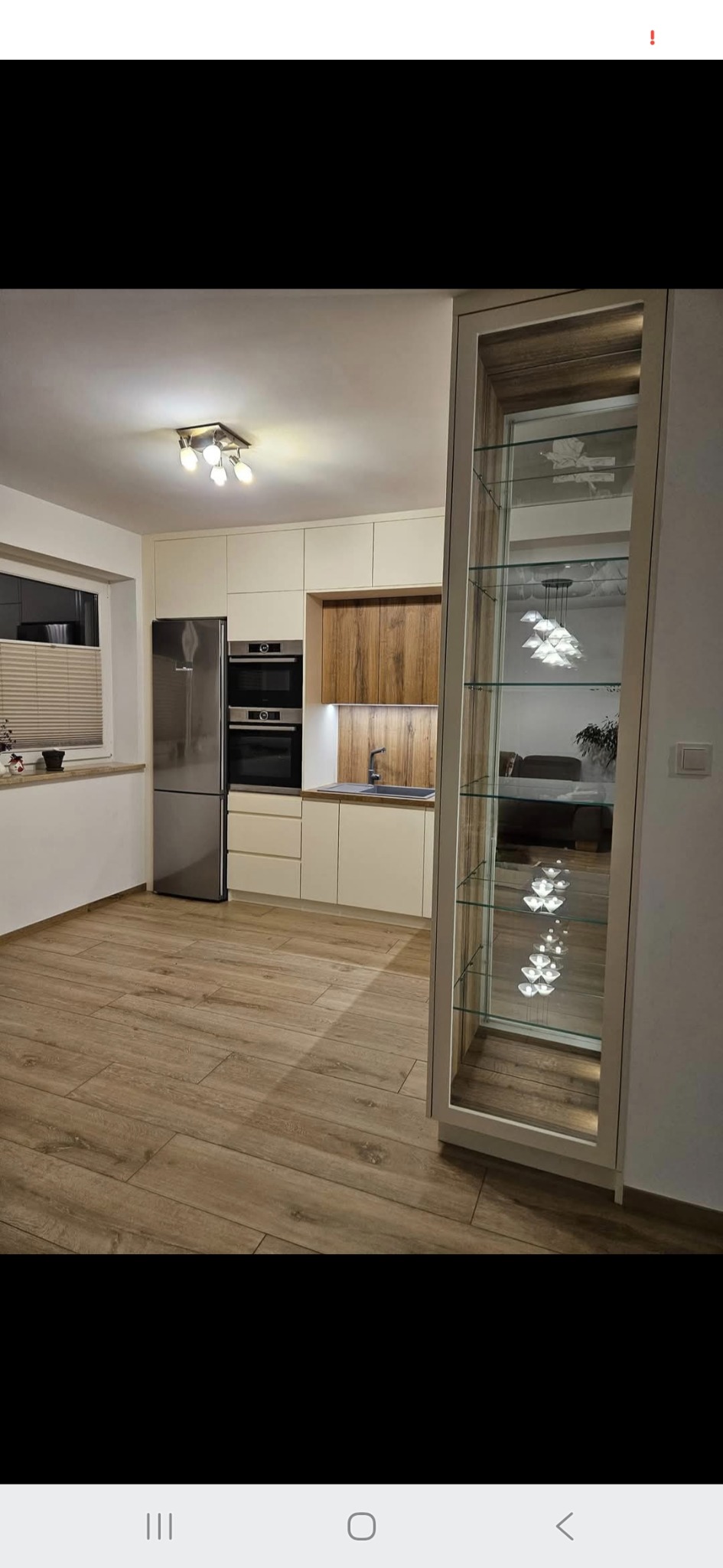 Jasna kuchnia z drewnianymi akcentami i przeszkloną witryną w Chojnicach. Nowoczesny design, widoczne sprzęty AGD i drewniana podłoga.