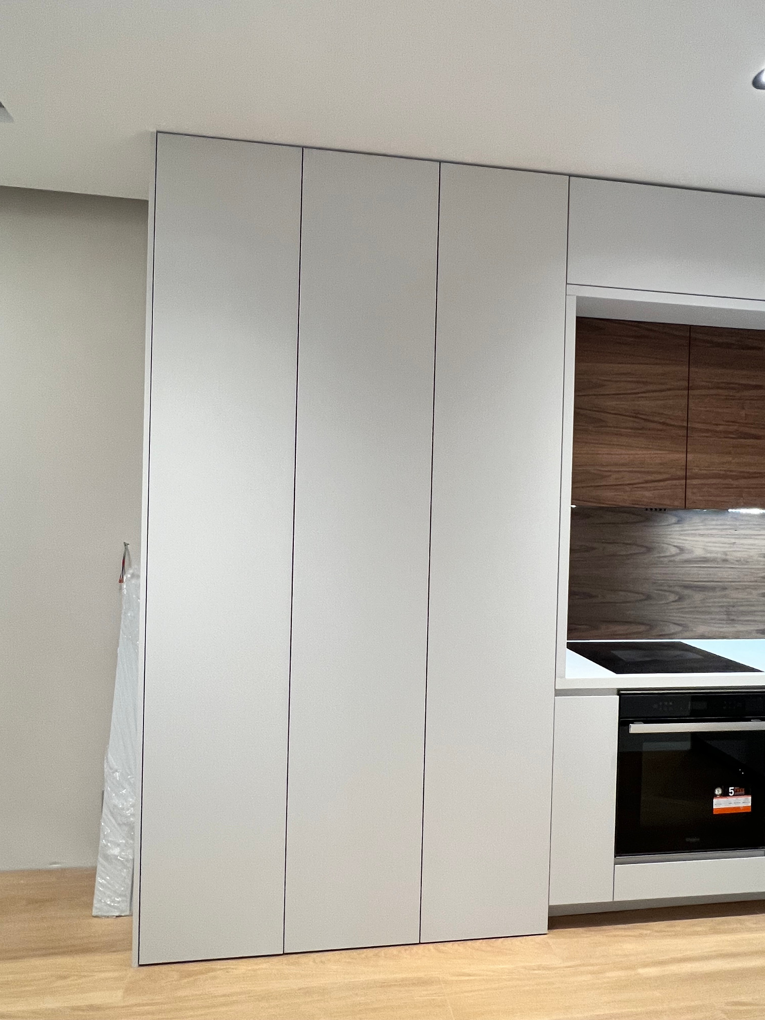 Minimalistyczna zabudowa kuchenna w Słupnie: wysokie, matowe, szare szafki z frontami bez uchwytów, piekarnik w zabudowie i drewniane wykończenie w tle.