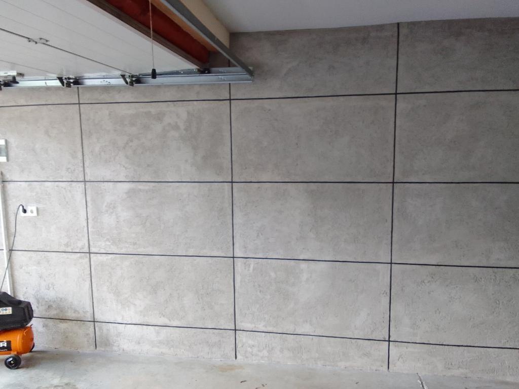 Ściana garażu wykończona płytami imitującymi beton, z widocznymi czarnymi fugami i kompresorem powietrza w rogu