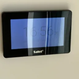 Panel sterowania systemu alarmowego Satel zamontowany na ścianie, wyświetlający aktualny czas i datę.