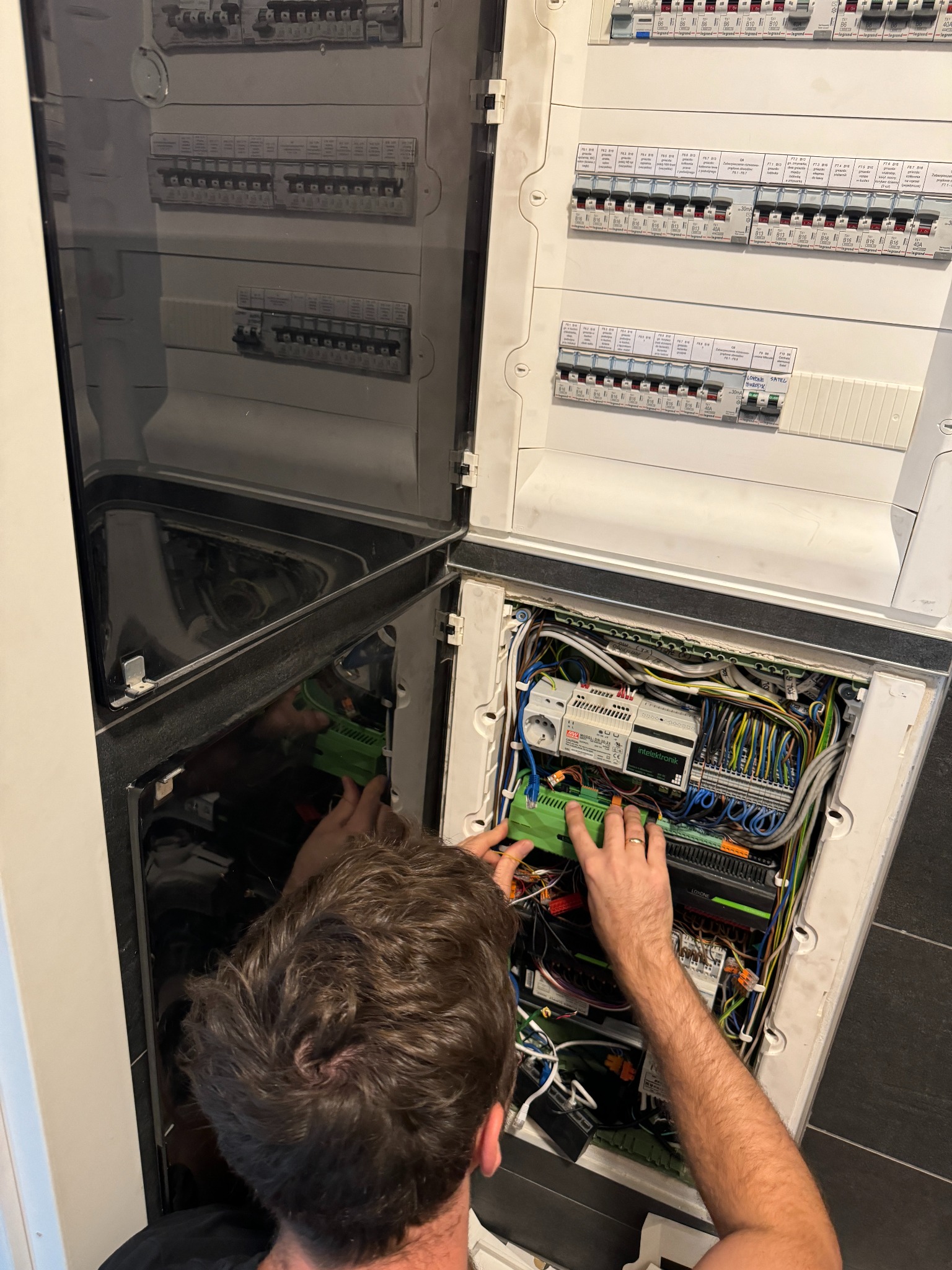 Elektryk instaluje moduł w szafie rozdzielczej, widoczne przewody, listwy zaciskowe i elementy automatyki, szafa zamykana na zatrzask.