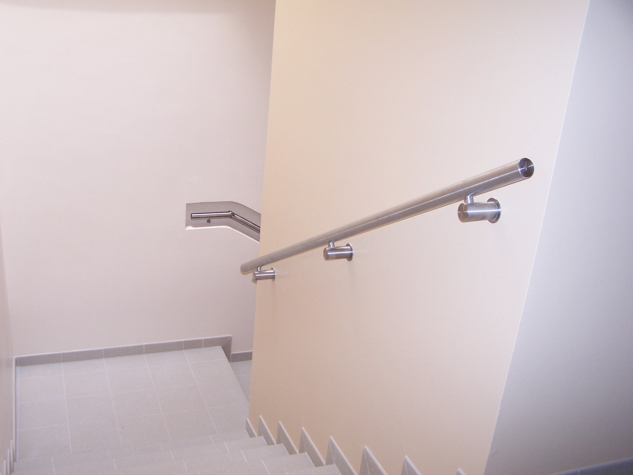 Pochwyt przyścienny ze stali nierdzewnej zamontowany na ścianie przy schodach, widok z góry na dół.