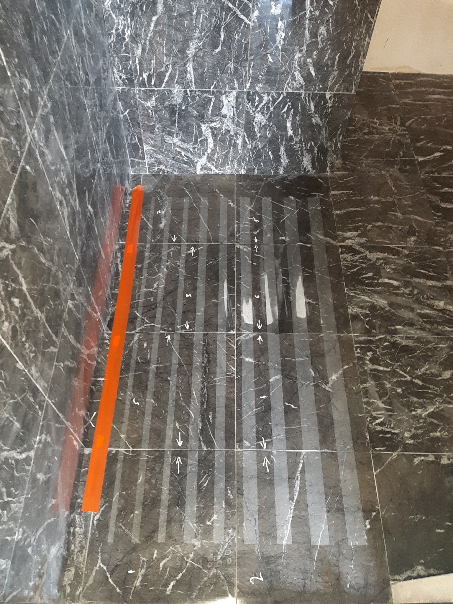 Ciemna marmurowa podłoga z zaznaczonymi liniami cięcia płytek i kierunkiem ułożenia, pomarańczowy profil przyścienny.