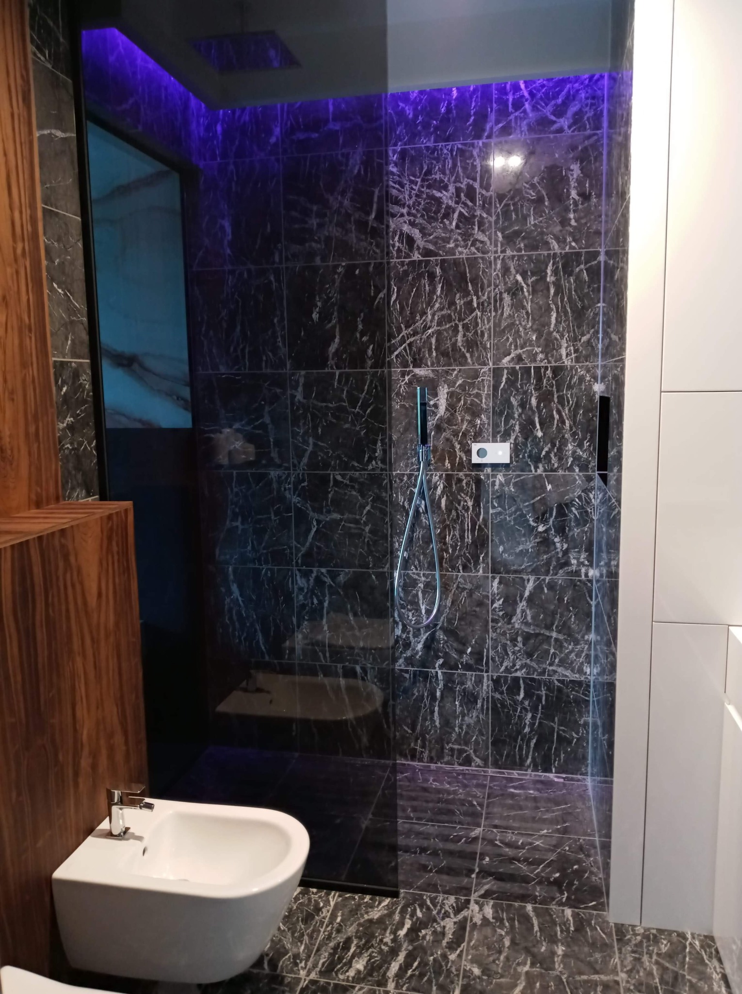 Nowoczesna łazienka w Lublinie z kabiną prysznicową typu walk-in wykończoną czarnymi płytkami imitującymi marmur, podświetleniem LED w suficie i wiszącym bidetem.