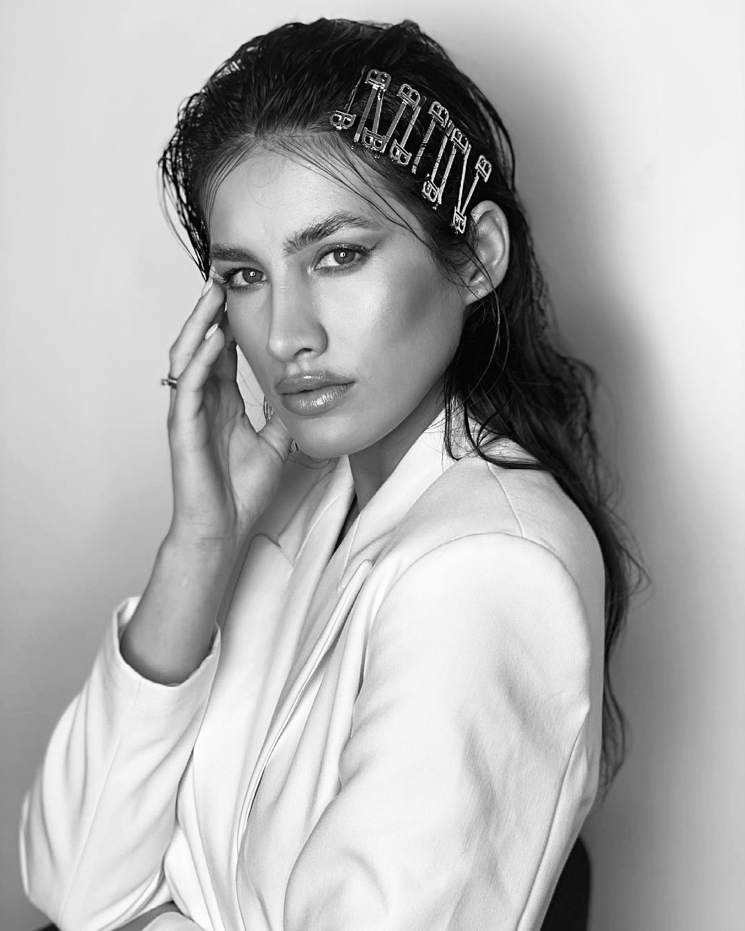 Portret kobiety w białym żakiecie z mokrymi włosami, upiętymi metalowymi spinkami z literami, delikatny makijaż.