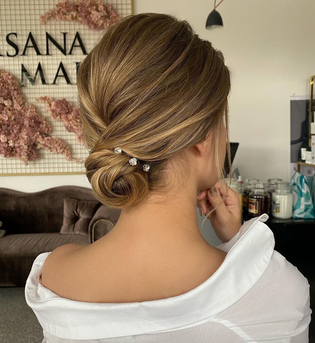 Upięcie włosów w kok z wpiętymi ozdobnymi spinkami w kształcie kwiatów, widok z tyłu na tle salonu.