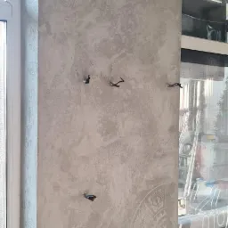 Ściana pokryta dekoracyjnym tynkiem strukturalnym w odcieniach szarości z delikatnymi, rozmytymi wzorami przypominającymi mandale, widoczne wystające kable elektryczne przed zamontowaniem osprzętu.