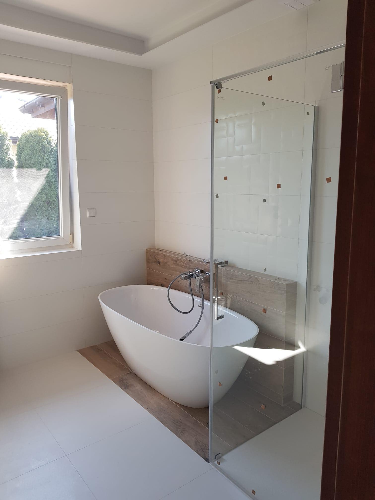 Nowoczesna łazienka z wolnostojącą wanną, przeszkloną kabiną prysznicową i białymi płytkami z dekoracyjnymi, małymi, brązowymi kwadratami.