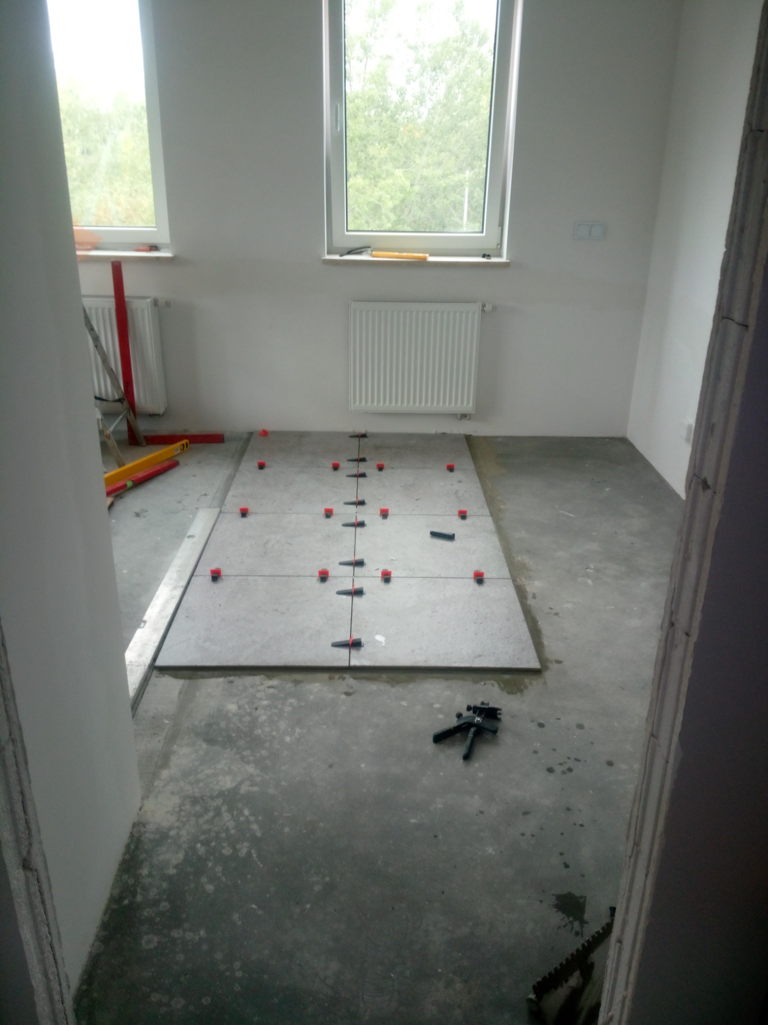 Układanie szarych płytek na podłodze w trakcie remontu łazienki, widoczne poziomice, krzyżyki dystansowe i narzędzia glazurnicze.