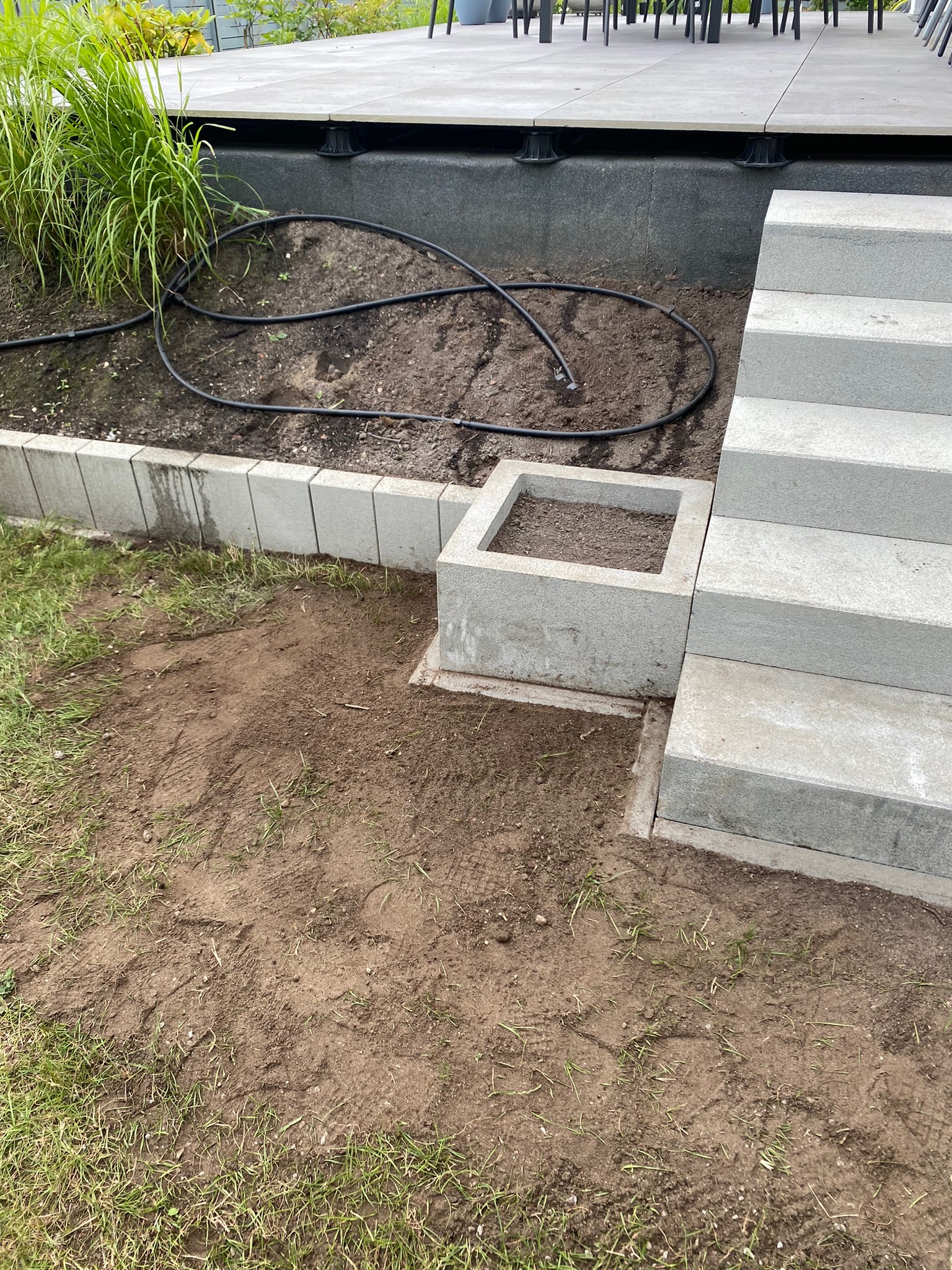 Przygotowany teren pod nasadzenia z obrzeżem z kostki, schodami betonowymi i systemem nawadniania.