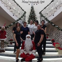 Selfcare Sonia Zgrabczyńska - Grupa kobiet i mężczyzna przebrany za Świętego Mikołaja pozują na schodach Hotelu Woinski Spa, ozdobionych świątecznymi dekoracjami, w tle choinka i ozdobny żyrandol.