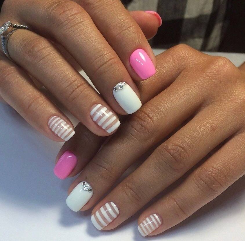 Dłonie z manicure w odcieniach bieli i różu, zdobione paskami i cyrkoniami, wykonane w salonie w Warszawie.