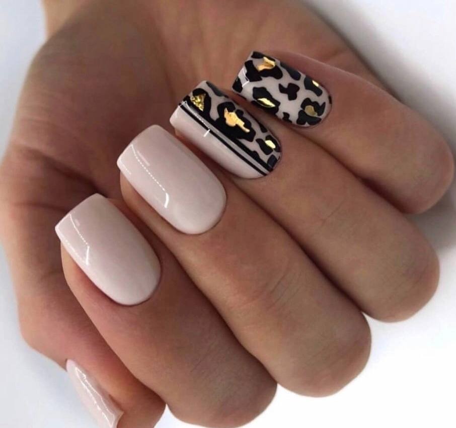 Dłoń z pomalowanymi paznokciami: dwa w kolorze jasnego różu, jeden z czarnymi paskami i złotymi akcentami, jeden z wzorem panterki i złotymi detalami.