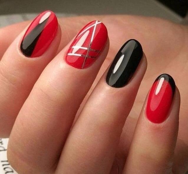 Dłoń z owalnymi paznokciami pomalowanymi na czerwono i czarno z geometrycznymi srebrnymi zdobieniami na jednym paznokciu.